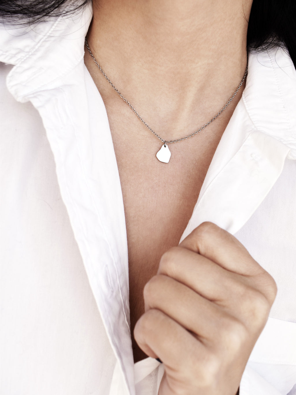Small silver organic-shaped pendant with chain on a woman's neck wearing a white shirt
