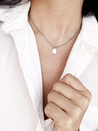Small silver organic-shaped pendant with chain on a woman's neck wearing a white shirt