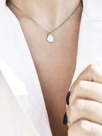 Small silver organic-shaped pendant with chain on a woman's neck wearing a white shirt