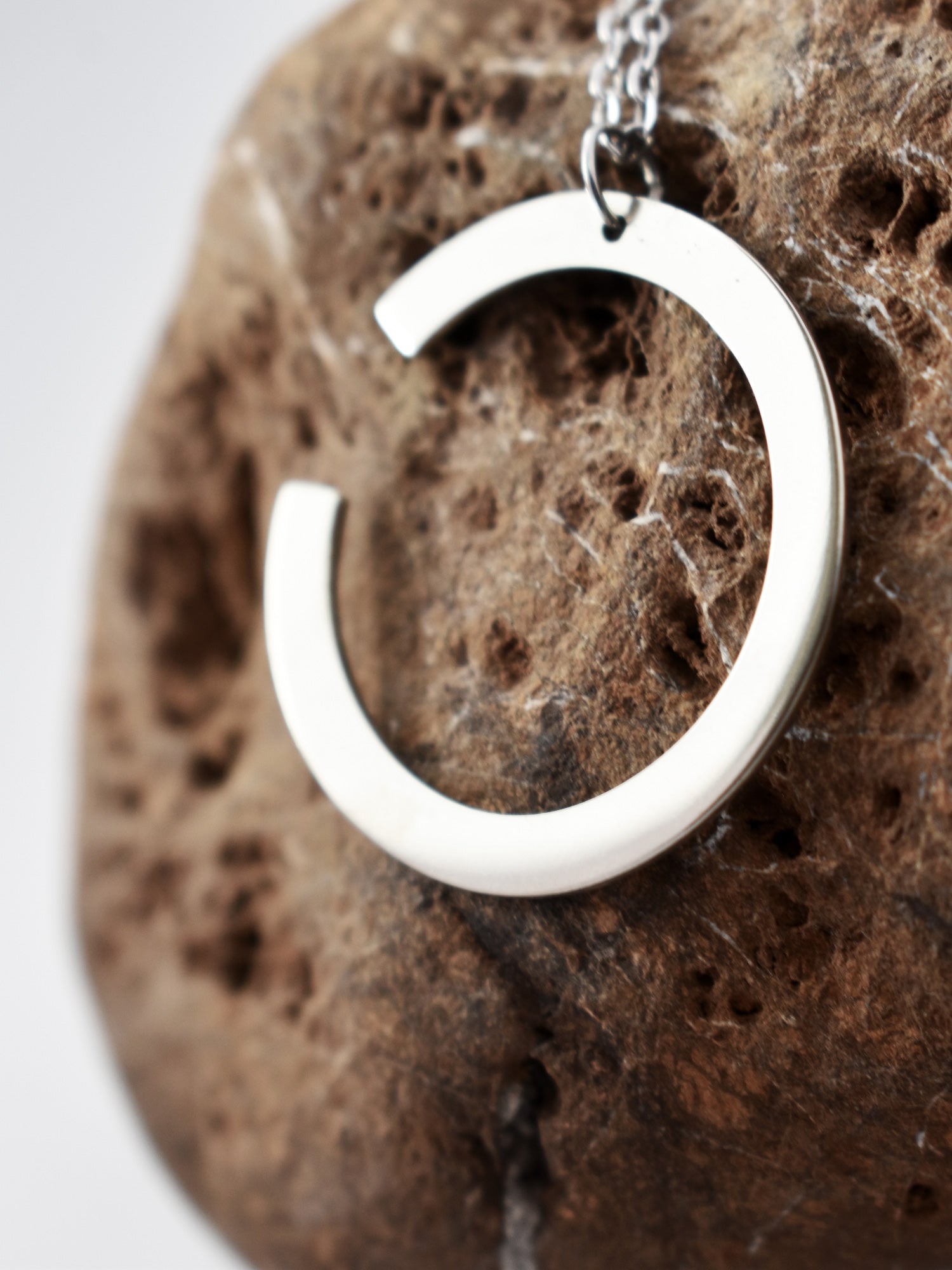 Close-up of silver crescent-shaped pendant with chain on a textured brown stone
