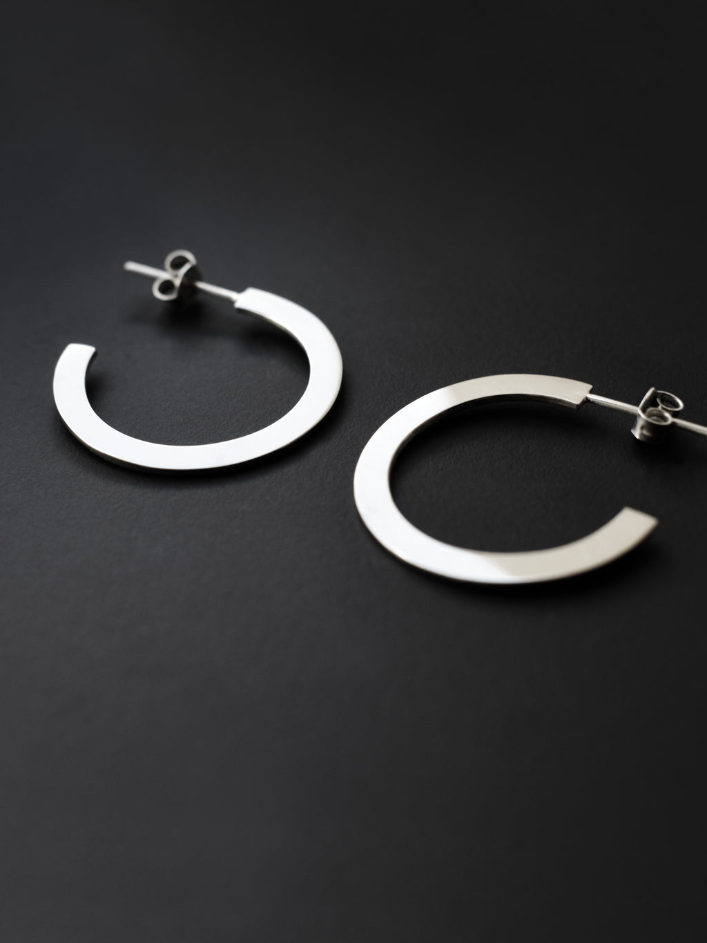 Close-up of pair of silver hoop earrings on a black background