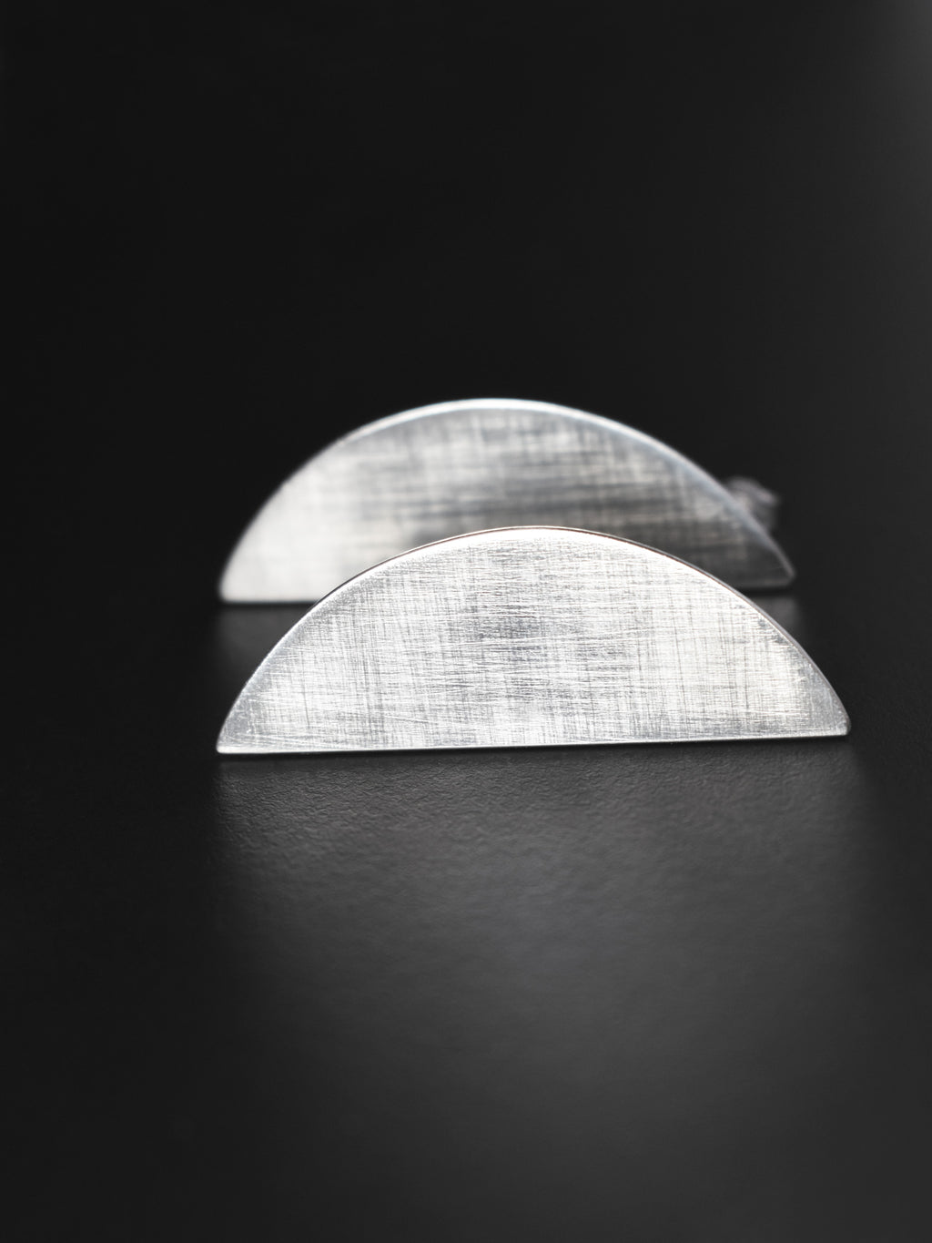 Pair of brushed silver semicircle stud earrings on a black background