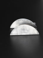 Pair of brushed silver semicircle stud earrings on a black background