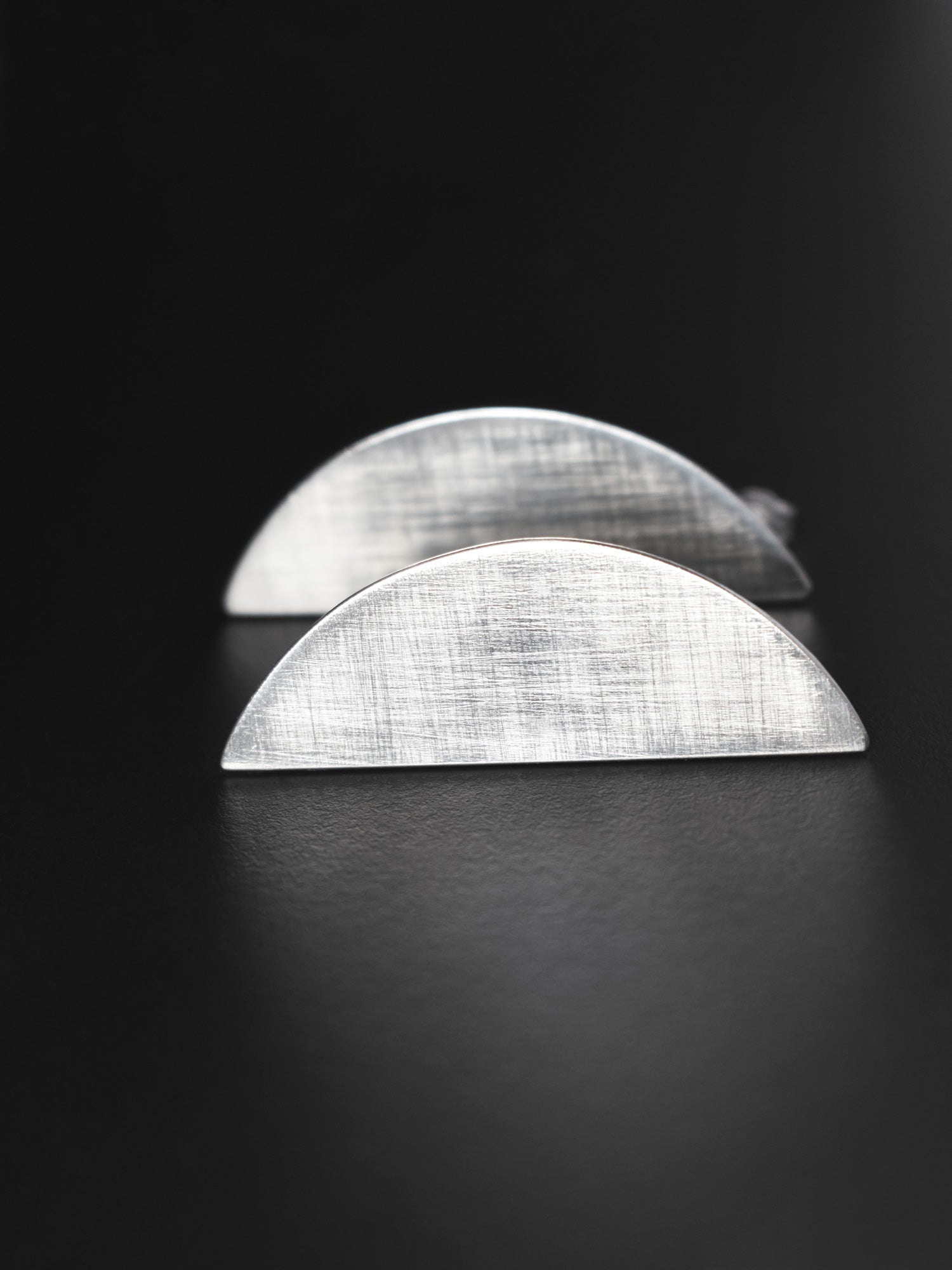 Pair of brushed silver semicircle stud earrings on a black background