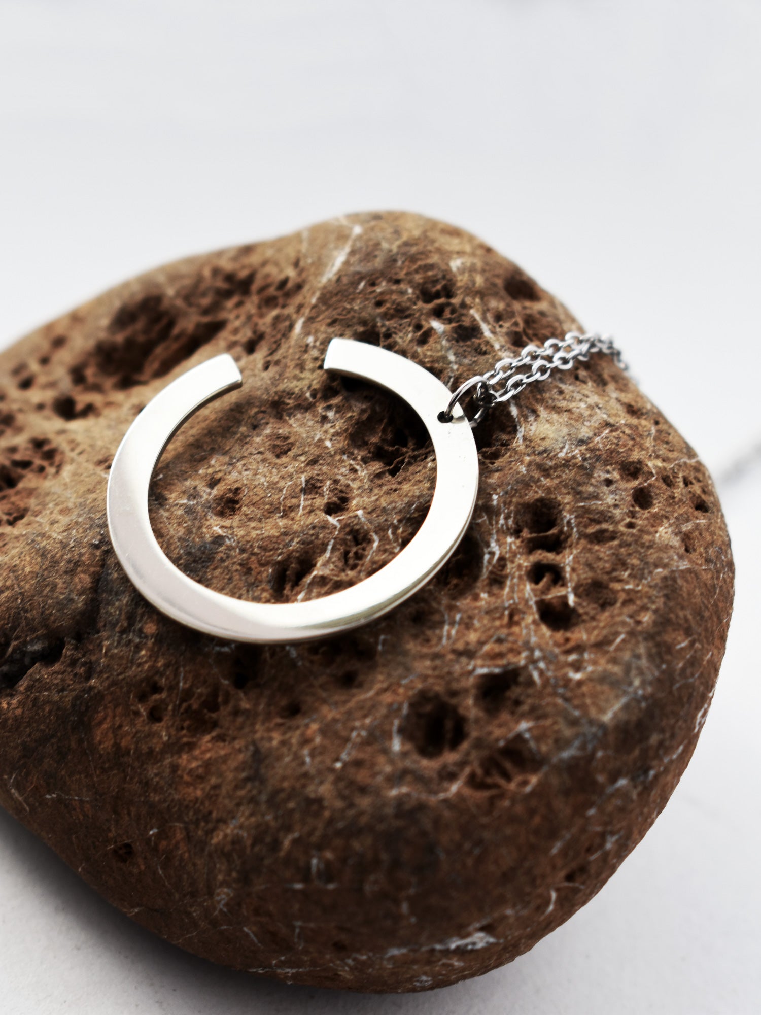 Silver crescent-shaped pendant with chain on a textured brown stone