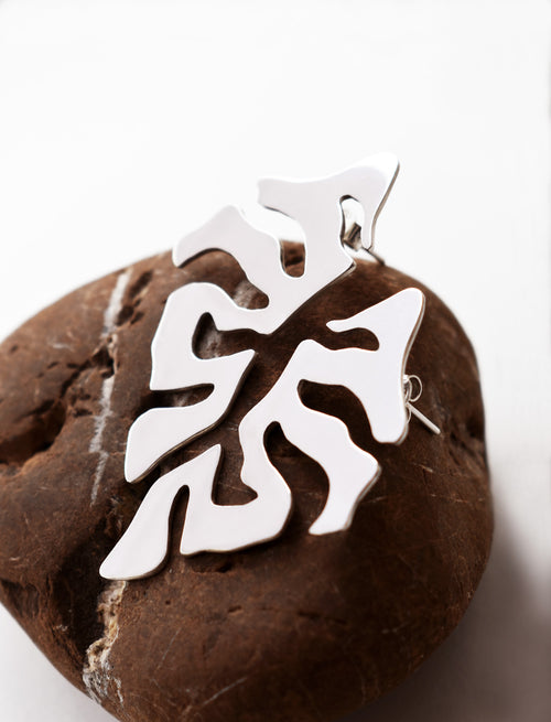 Pair of organic-shaped silver stud earrings with cutout details on a textured brown stone