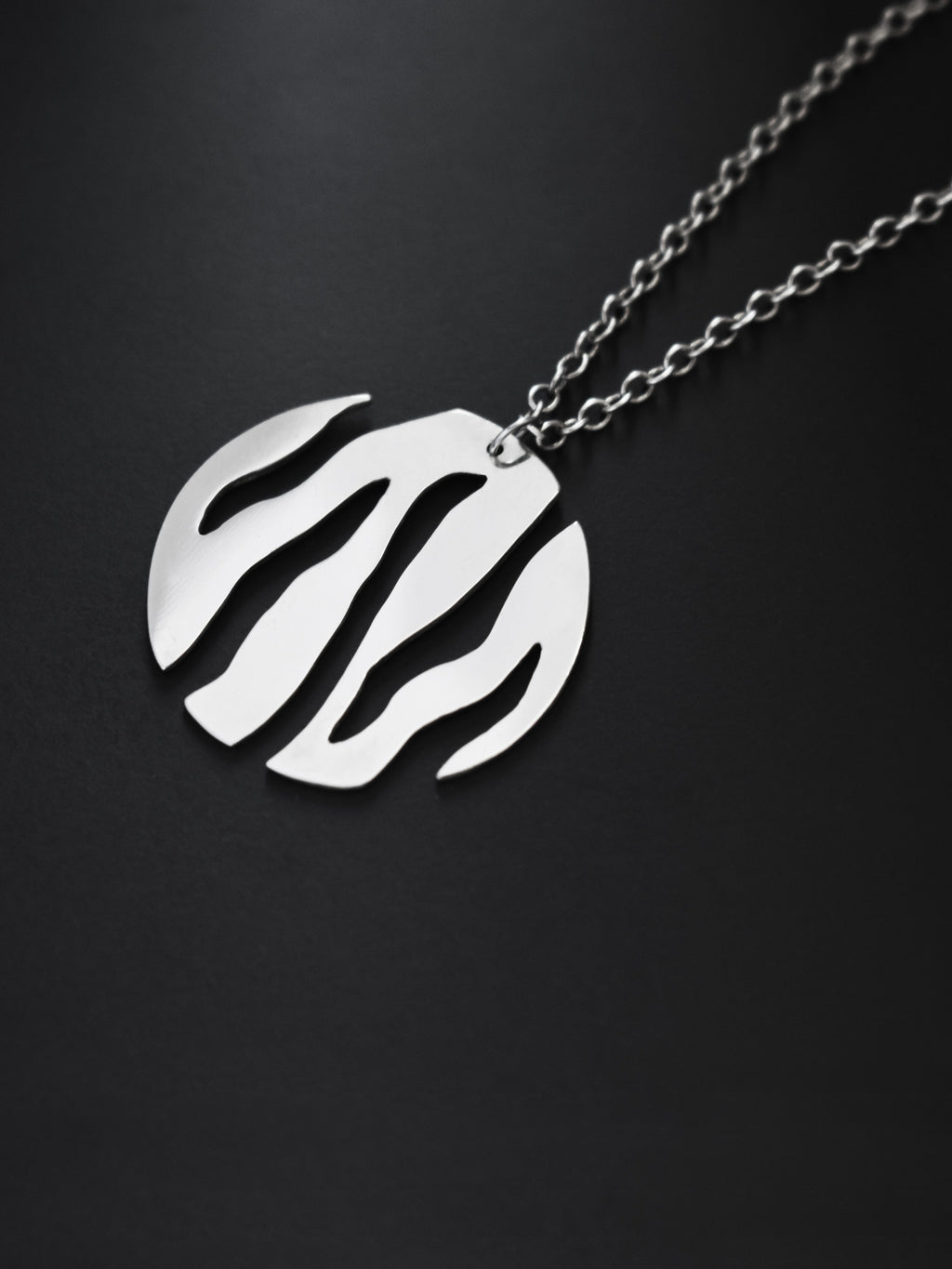 Close-up of a round silver pendant with flowing cutouts and chain on black background