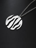 Close-up of a round silver pendant with flowing cutouts and chain on black background