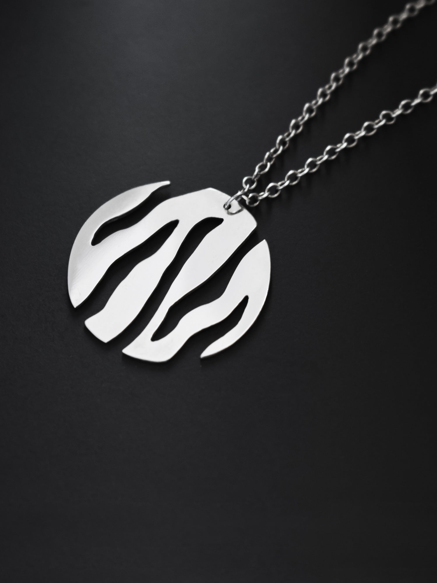 Close-up of a round silver pendant with flowing cutouts and chain on black background