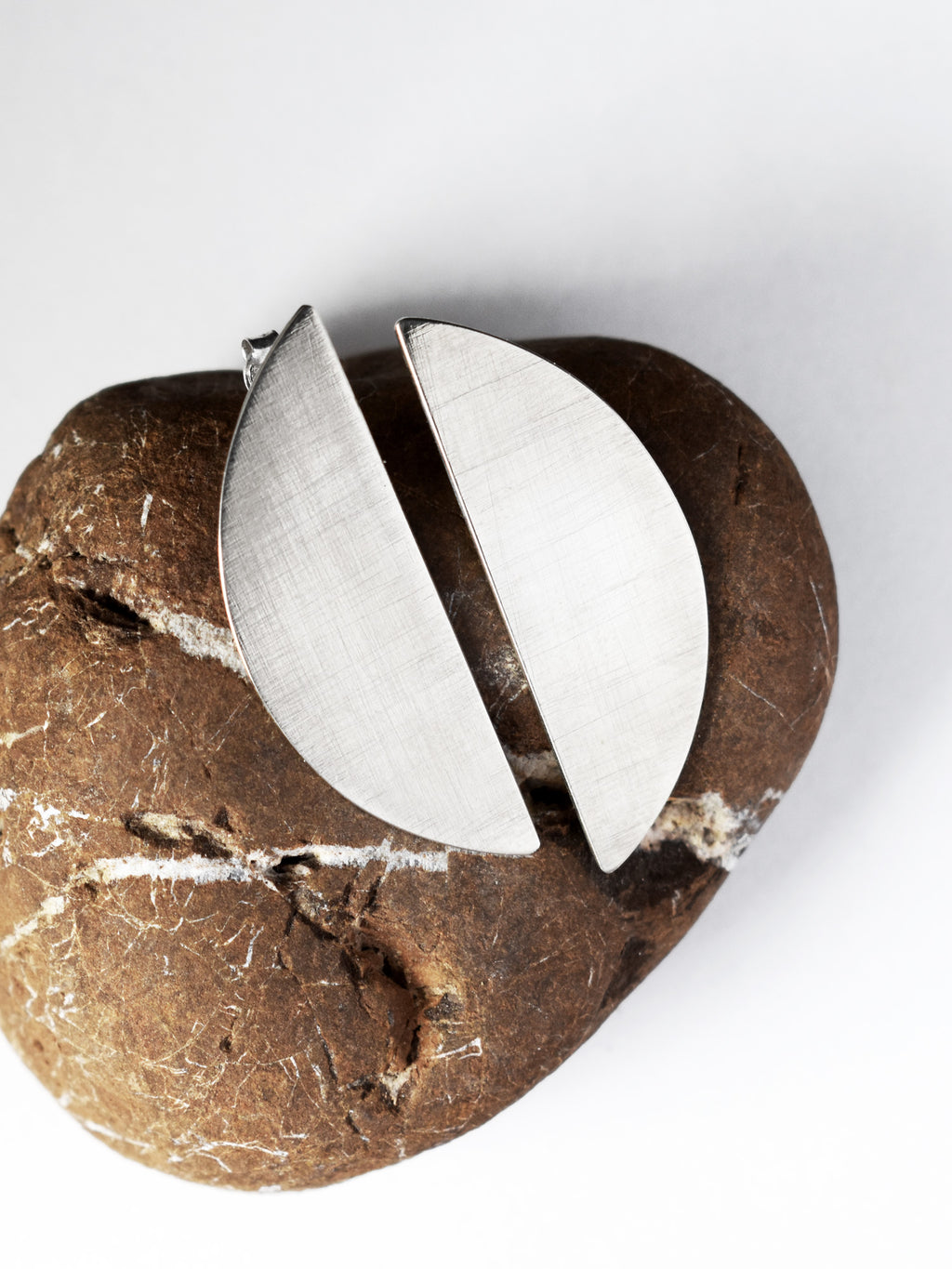 Pair of brushed silver semicircle stud earrings on a textured brown stone