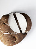 Pair of brushed silver semicircle stud earrings on a textured brown stone