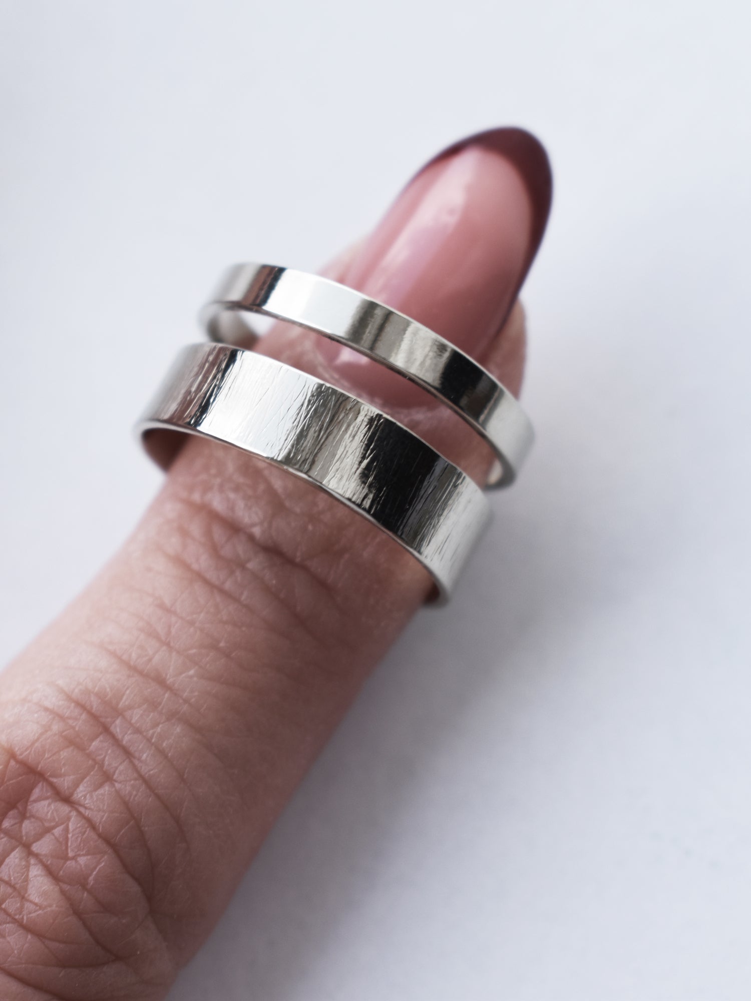 Adjustable double-band silver ring on a finger against a white background