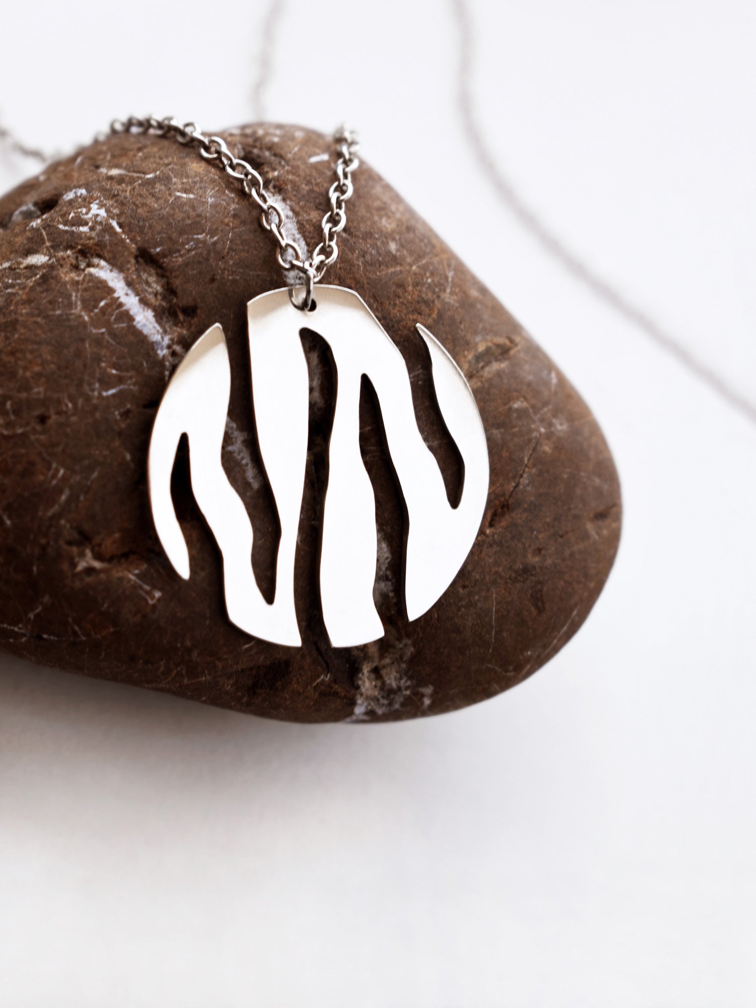 Close-up of a round silver pendant with flowing cutouts and chain on a textured brown stone