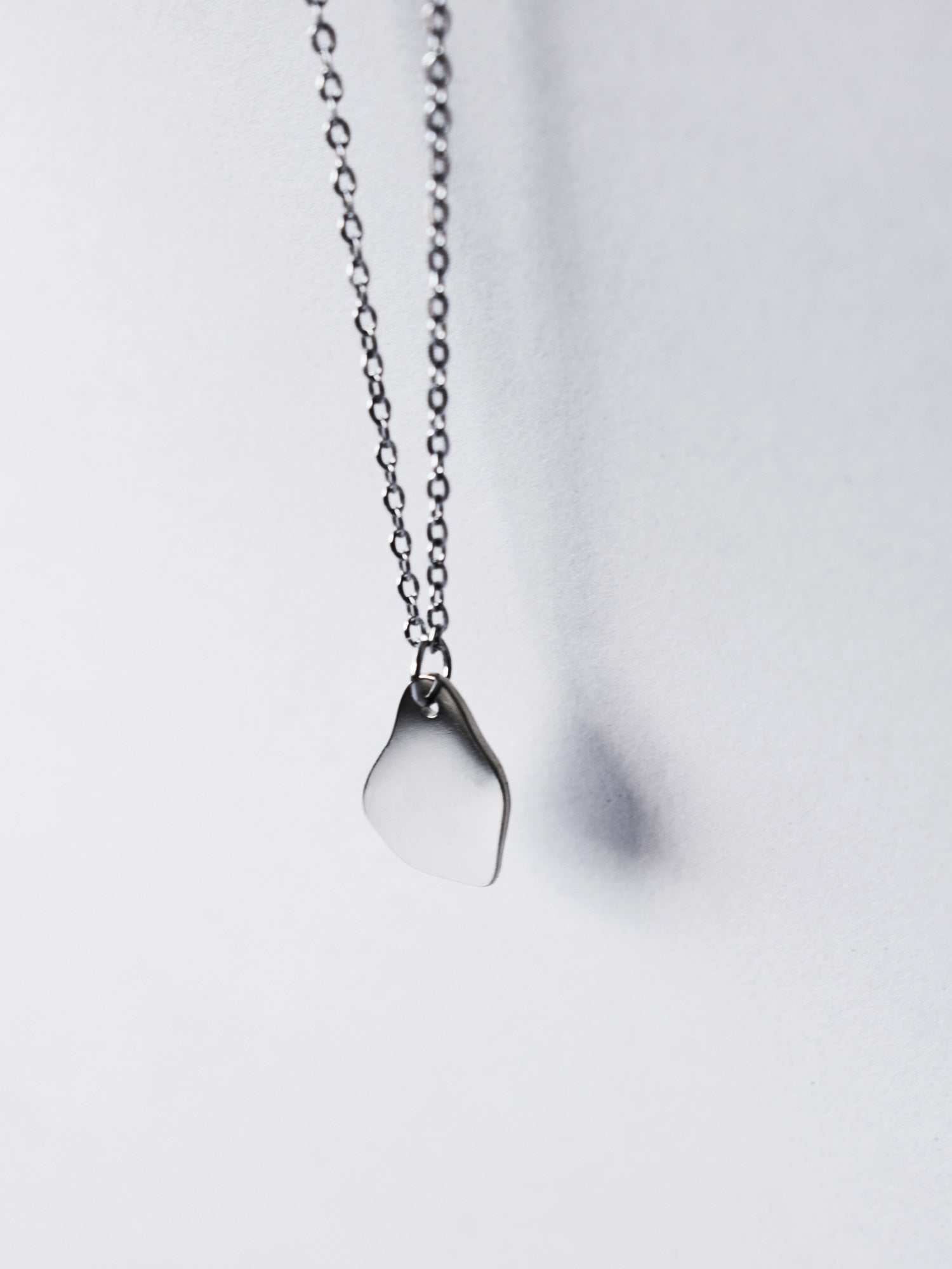 Small silver organic-shaped pendant with chain on a light grey background