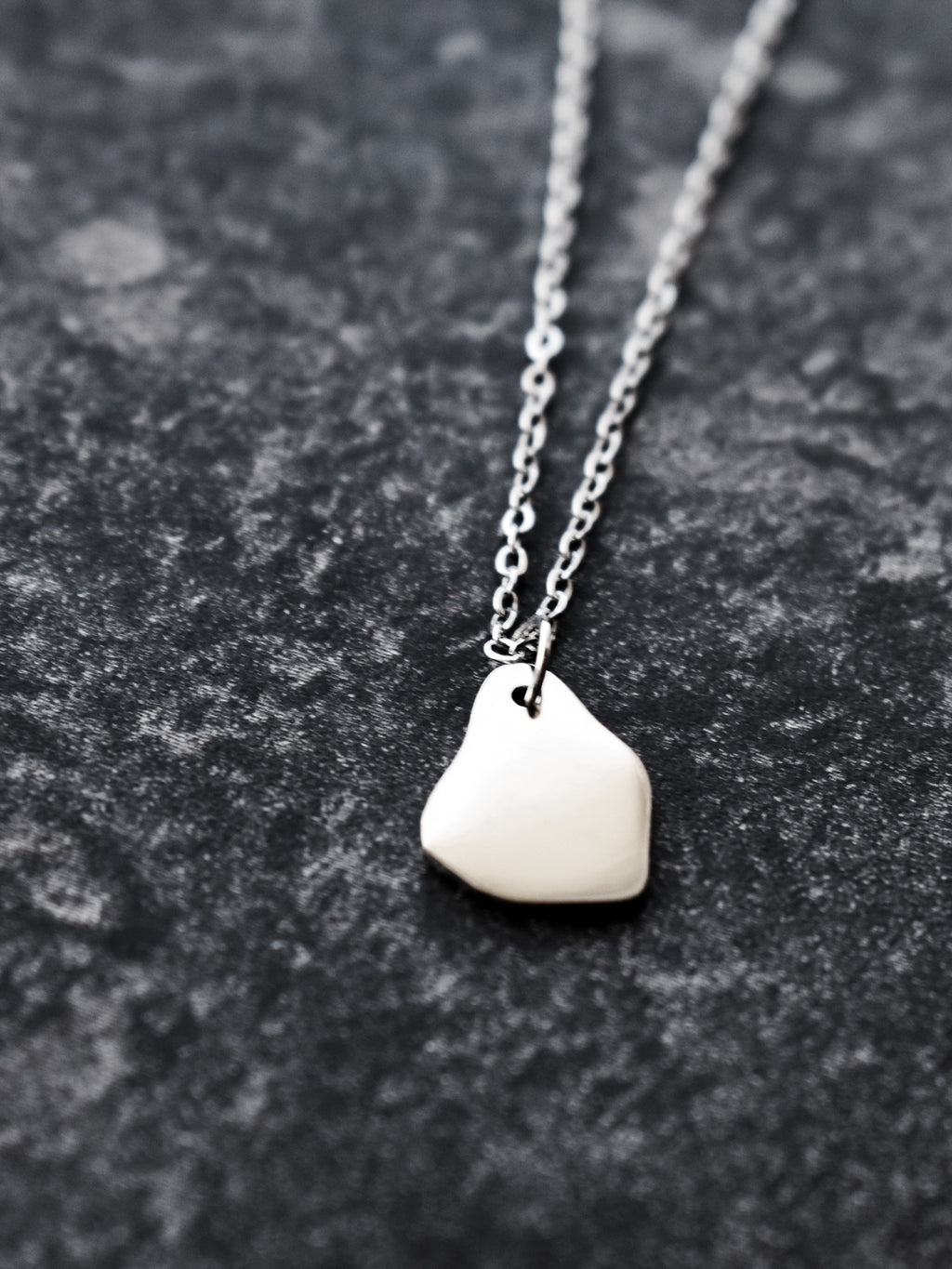 Close-up of a small silver organic-shaped pendant with chain on a dark textured surface