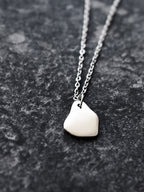 Close-up of a small silver organic-shaped pendant with chain on a dark textured surface