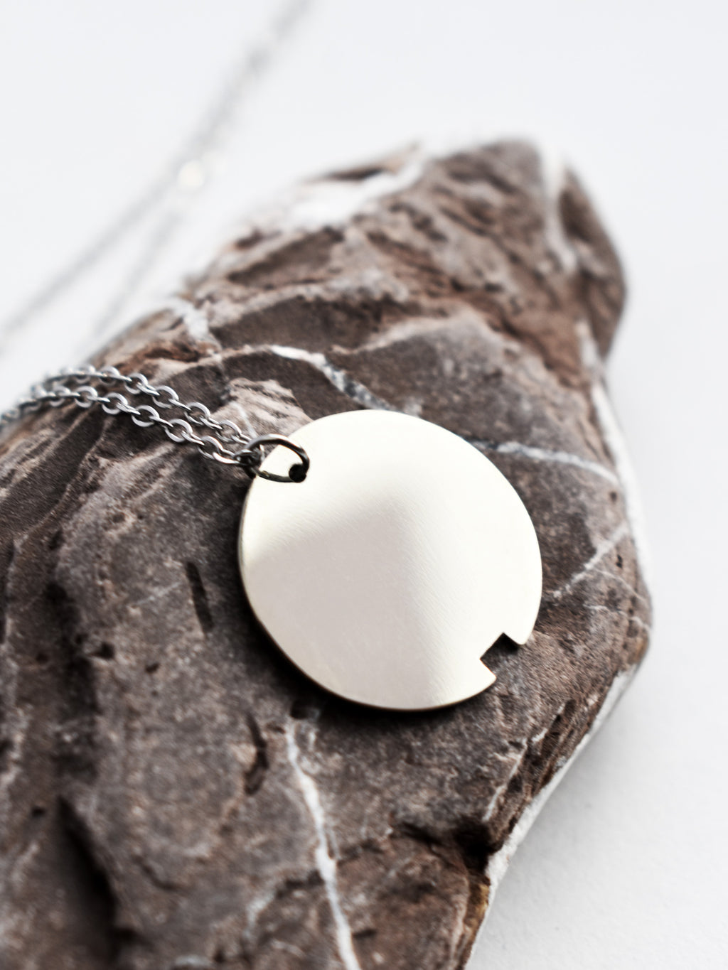Close-up of small silver circle pendant with chain on a dark stone