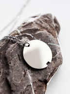 Close-up of small silver circle pendant with chain on a dark stone