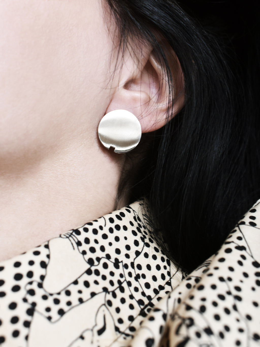 Close-up of a small circle silver stud earring worn by a woman