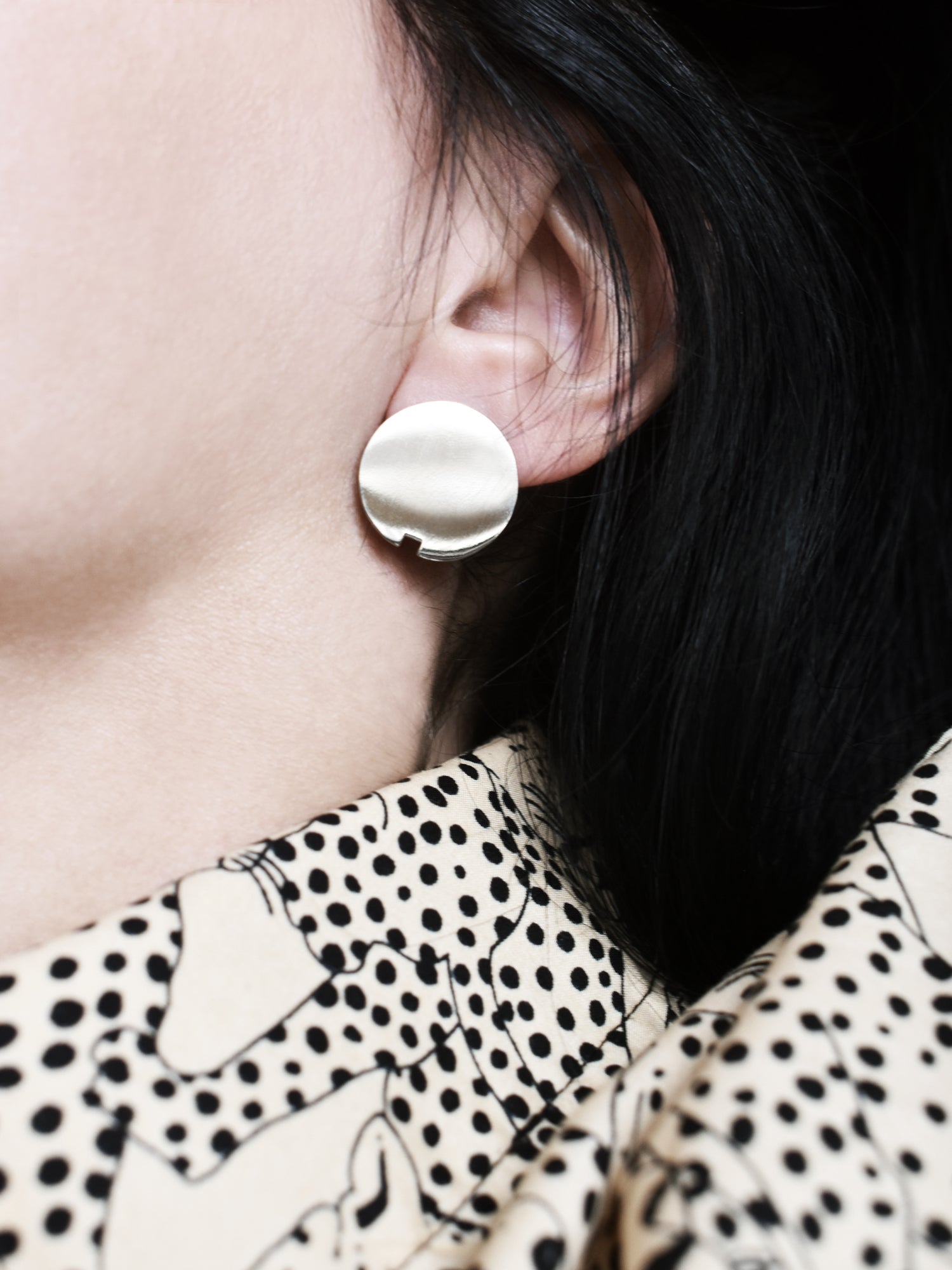 Close-up of a small circle silver stud earring worn by a woman