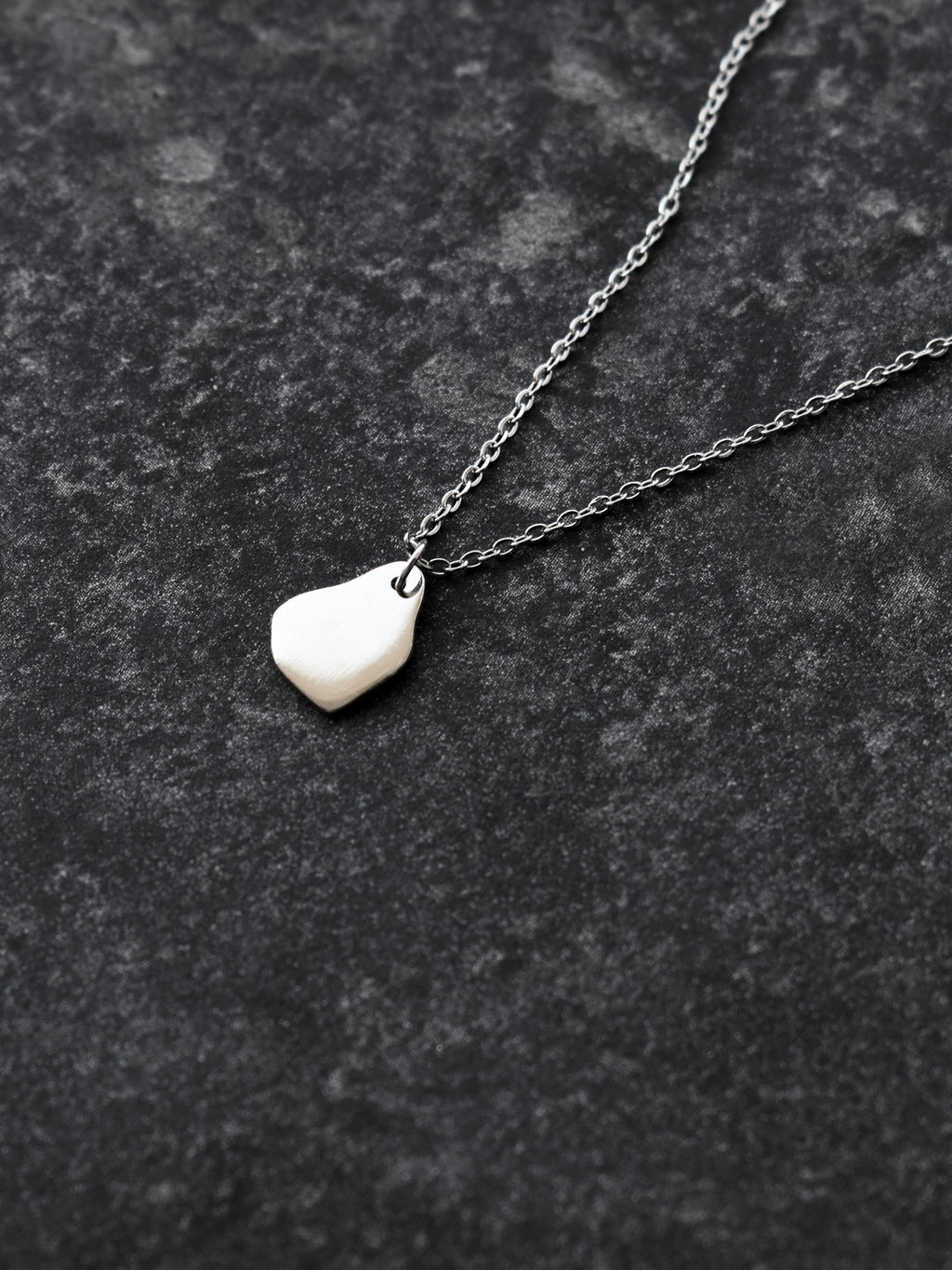 Small silver organic-shaped pendant with chain on a dark textured surface