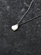 Small silver organic-shaped pendant with chain on a dark textured surface