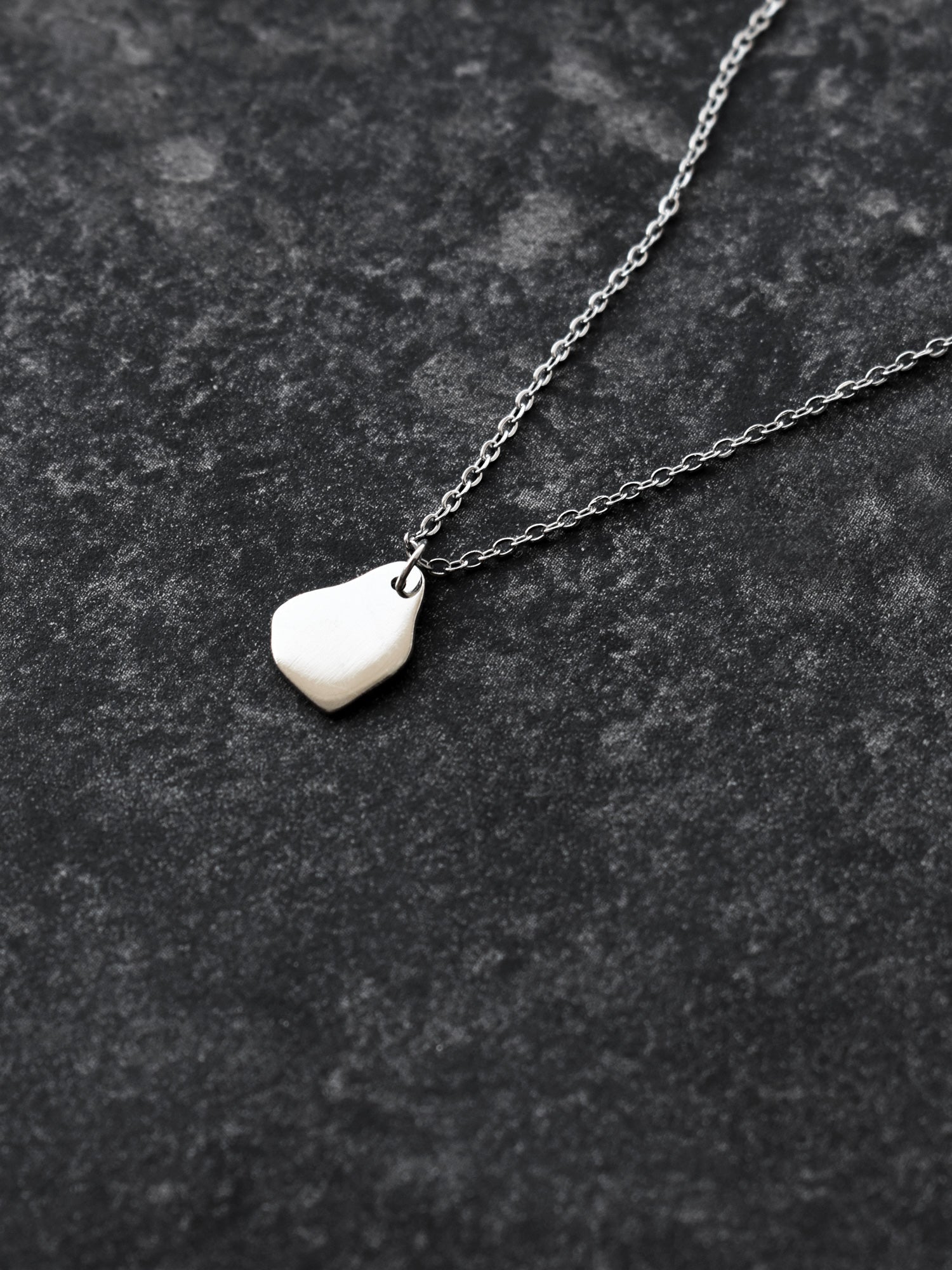 Small silver organic-shaped pendant with chain on a dark textured surface
