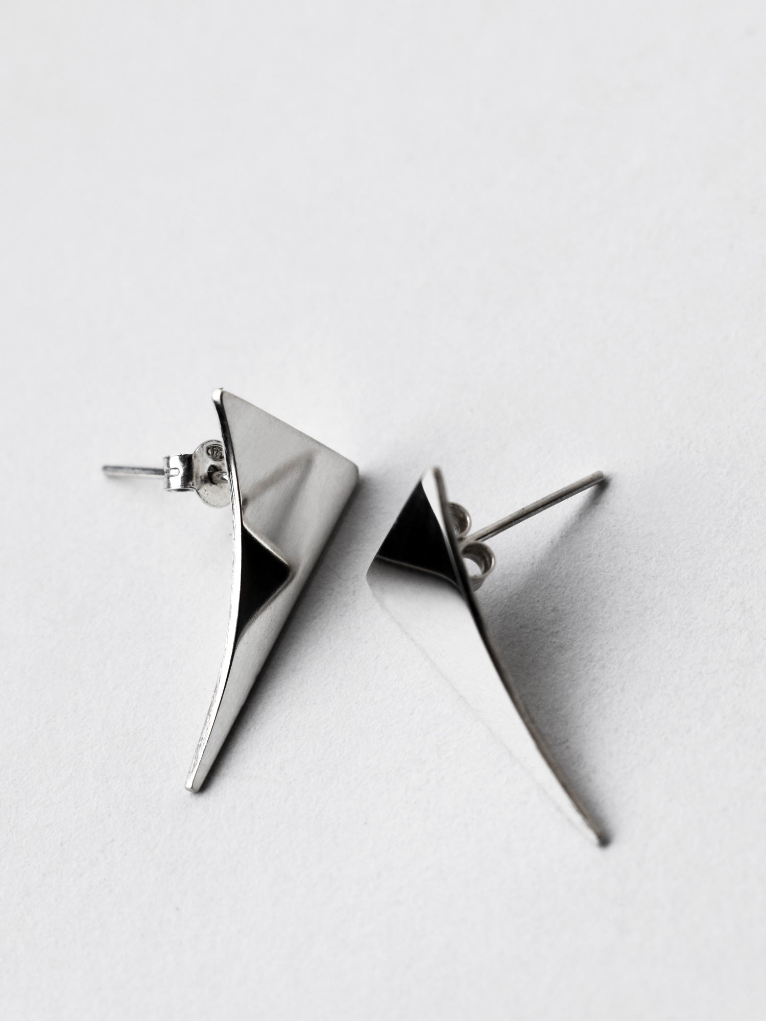 Pair of small curved triangular silver stud earrings on a light gray background