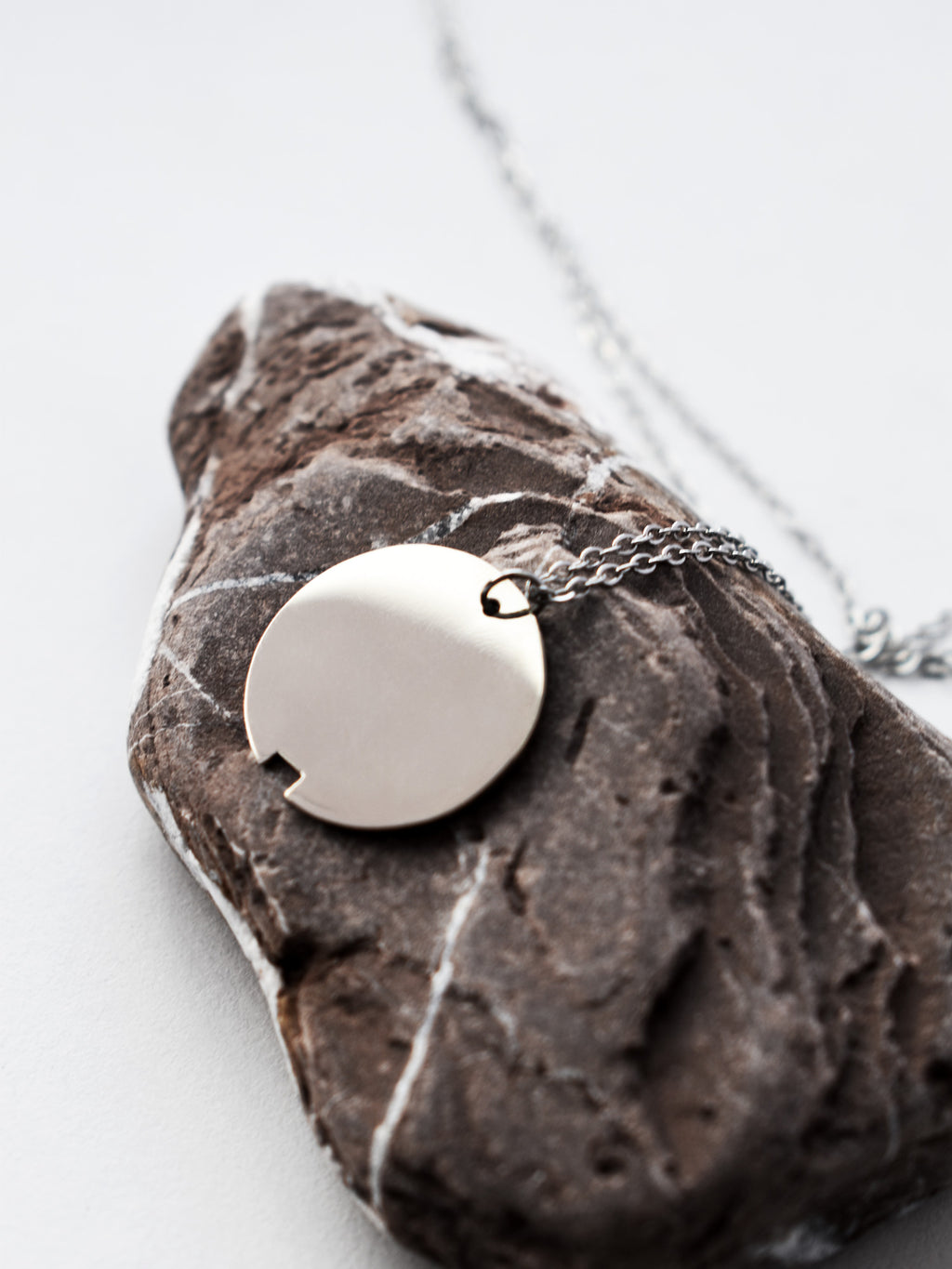 Small silver circle pendant with chain on a dark stone