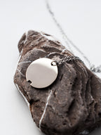 Small silver circle pendant with chain on a dark stone