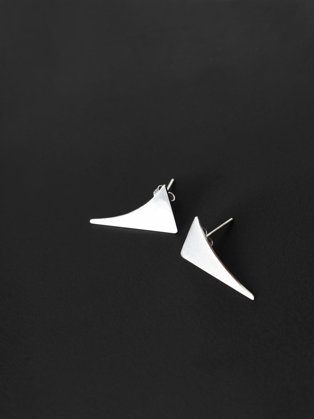 Pair of small curved triangular silver stud earrings on a black textured background