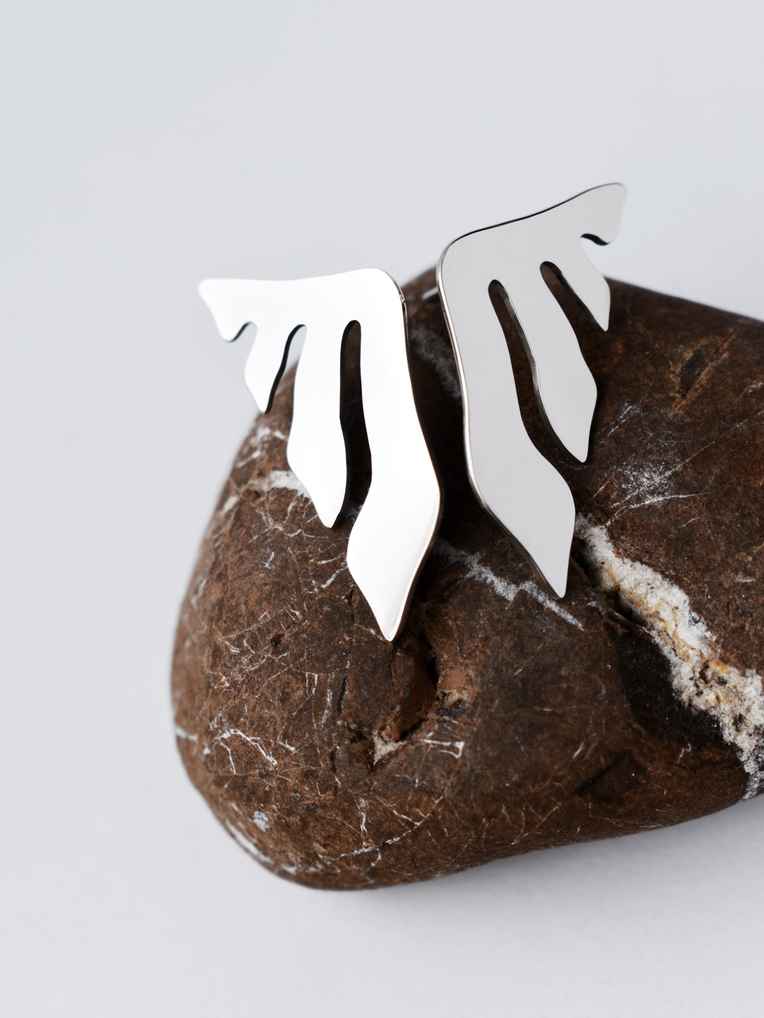 Pair of organic-shaped silver stud earrings with flowing cutouts on a textured brown stone