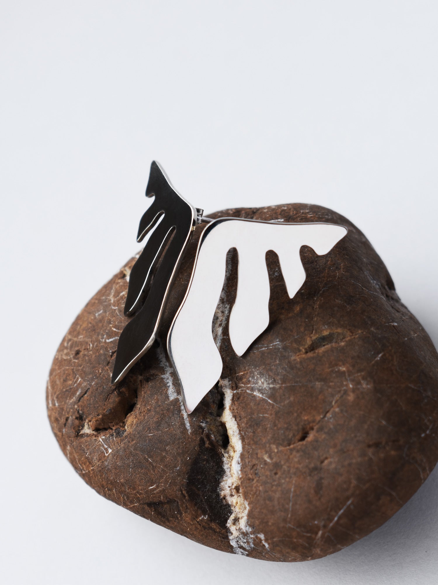 Pair of organic-shaped silver stud earrings with flowing cutouts on a textured brown stone