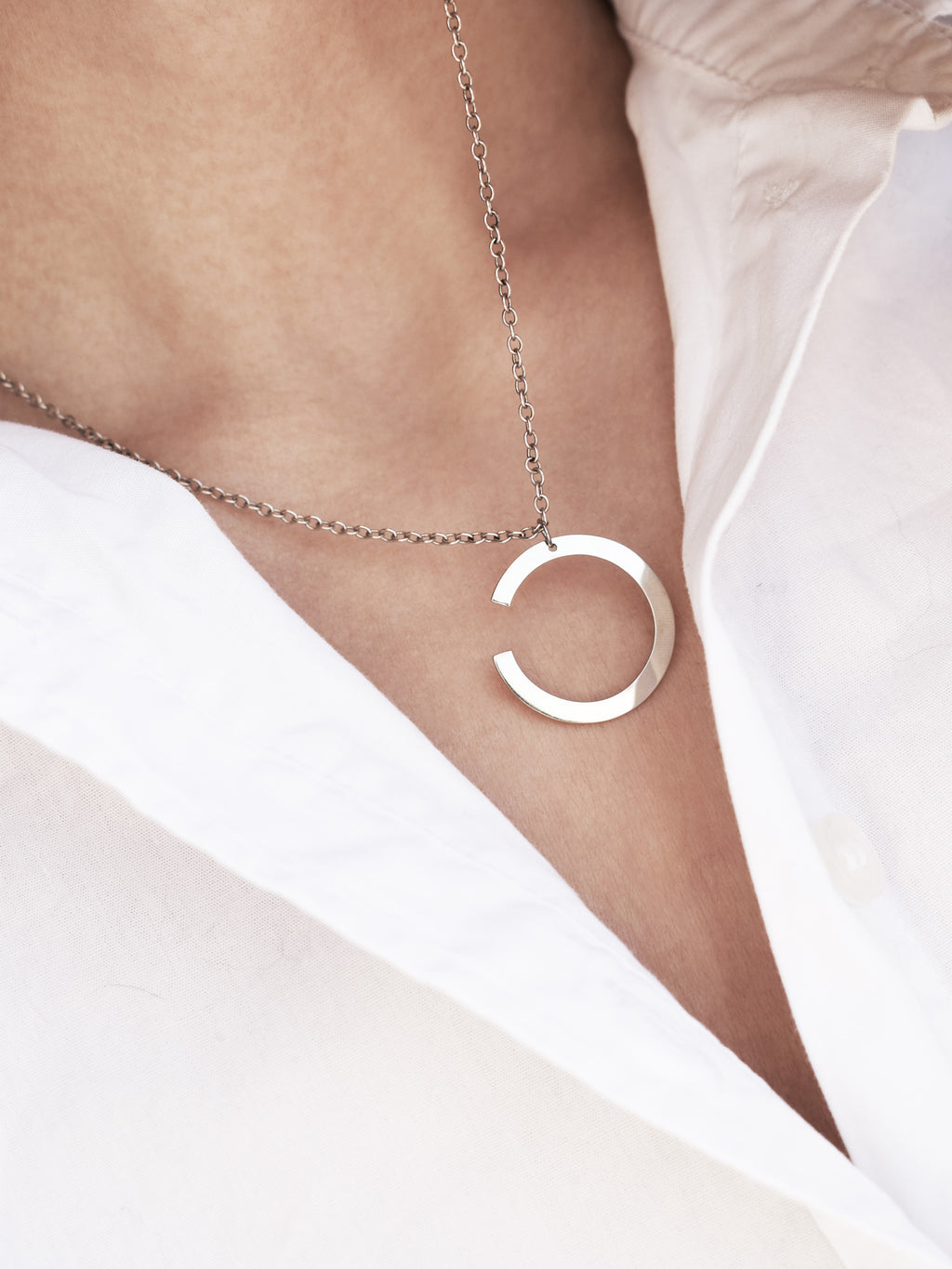 Silver crescent-shaped pendant with chain on a woman wearing a white shirt