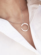Silver crescent-shaped pendant with chain on a woman wearing a white shirt