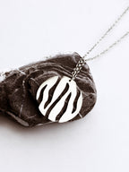 Round silver pendant with flowing cutouts and chain on a textured brown stone