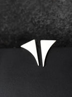 Pair of small curved triangular silver stud earrings on a black textured background