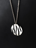 Round silver pendant with flowing cutouts and chain on black background