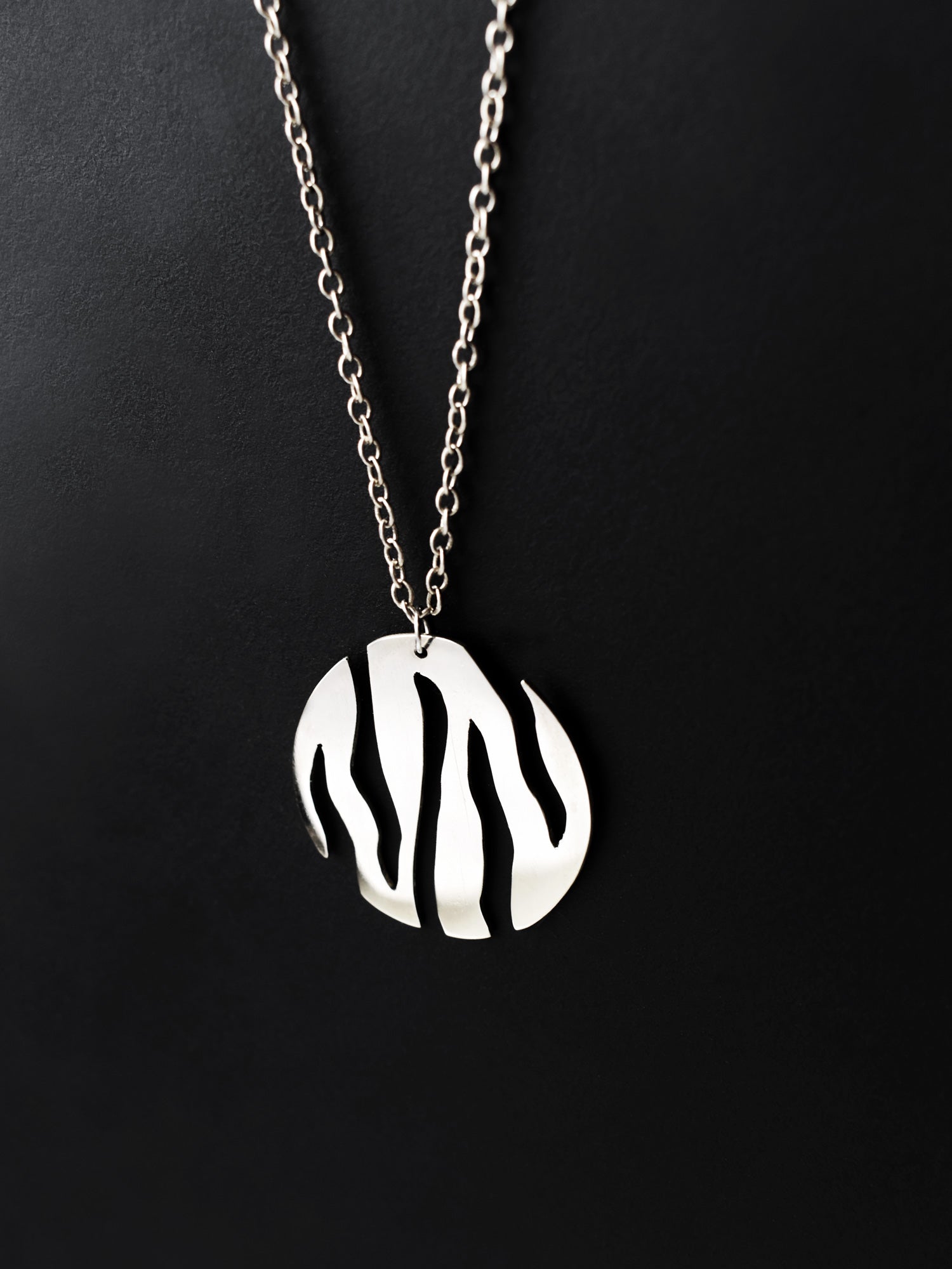Round silver pendant with flowing cutouts and chain on black background