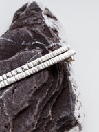 Pair of textured silver bar stud earrings on a textured stone surface