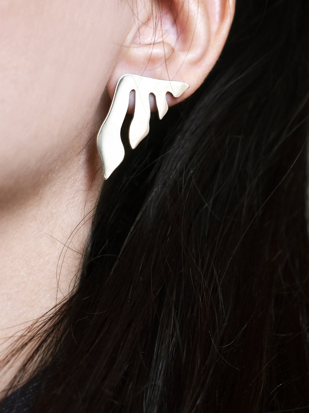Close-up of a woman wearing an organic-shaped silver stud earring with flowing cutouts