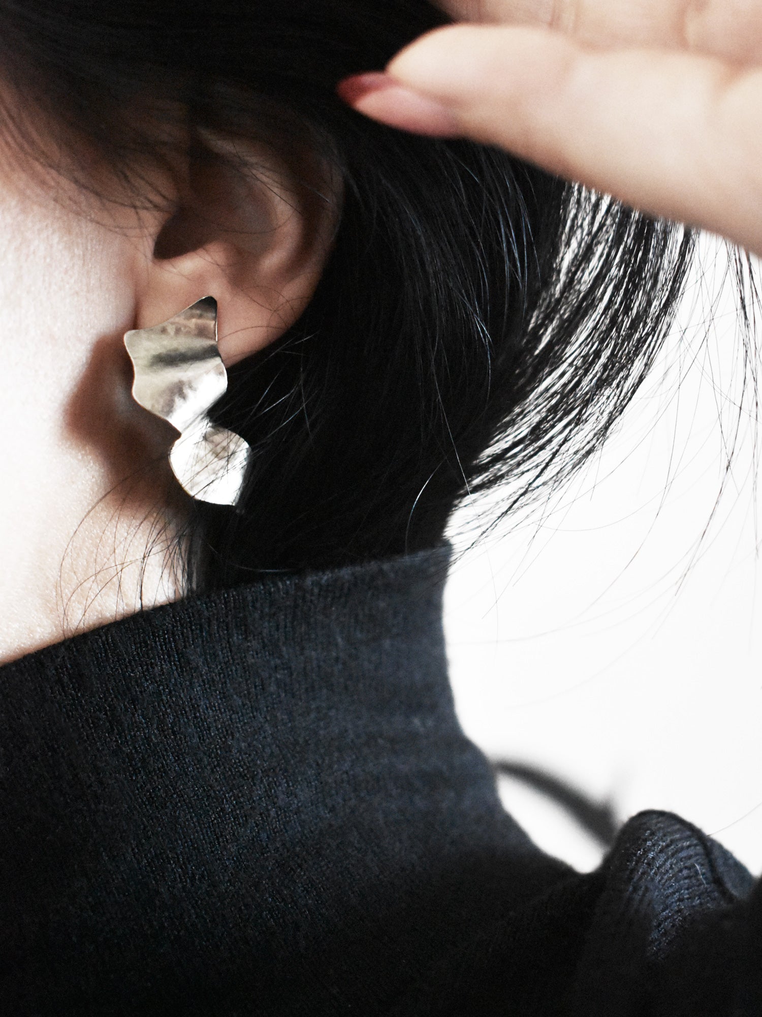 Close-up of a sculptural silver stud earring worn by a woman