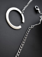 Close-up of silver crescent-shaped pendant with chain on a dark background