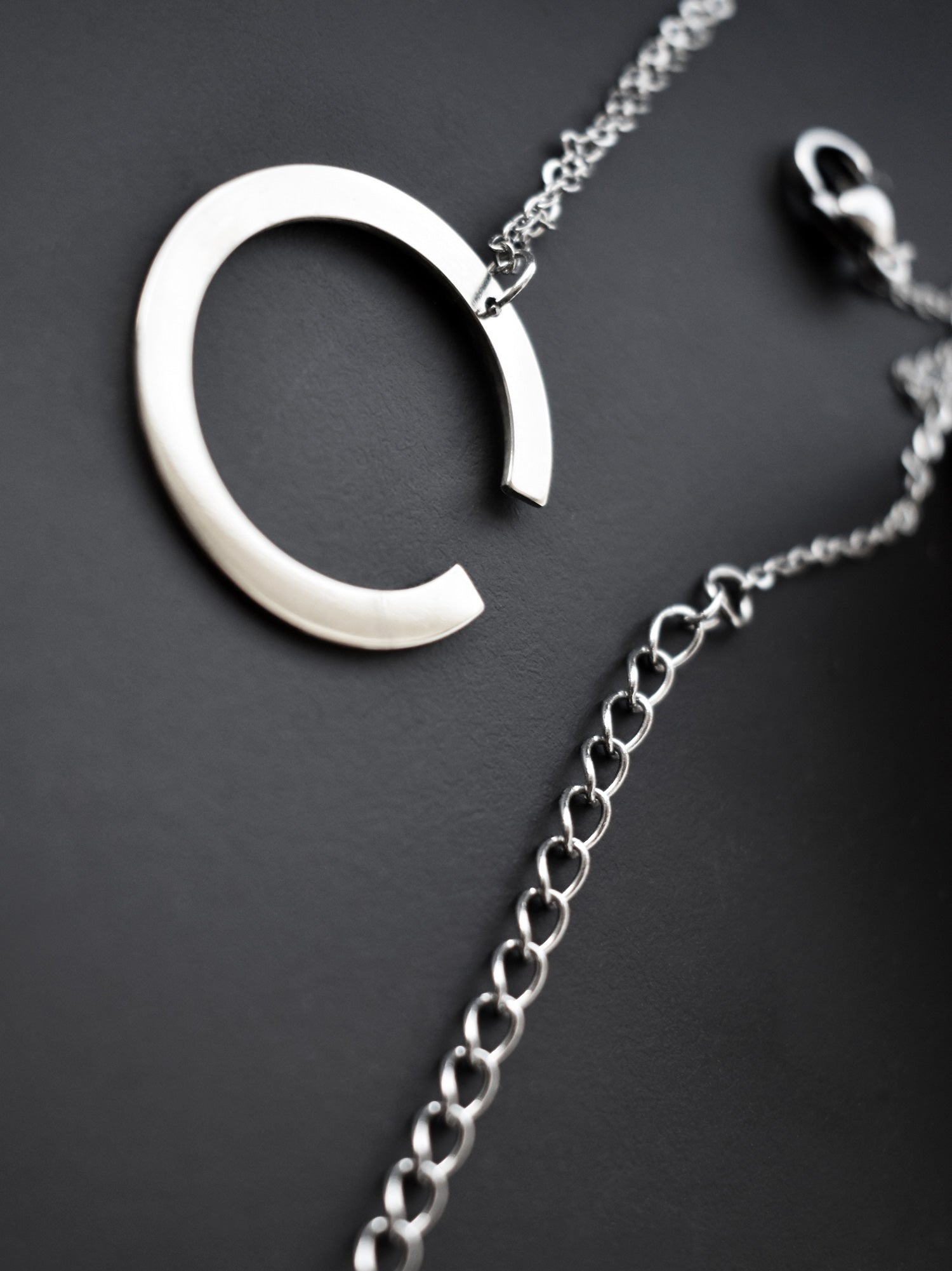Close-up of silver crescent-shaped pendant with chain on a dark background