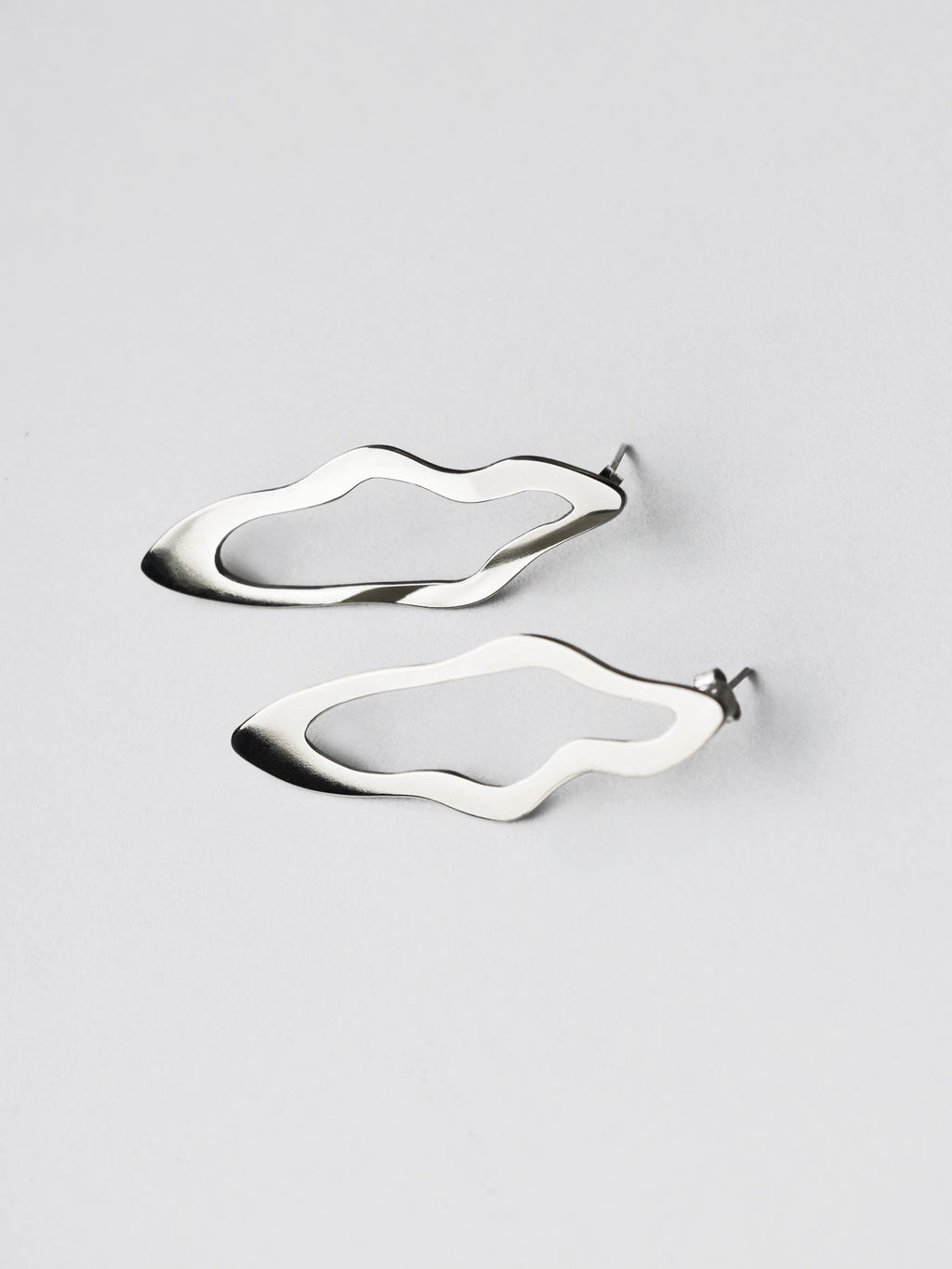 Pair of unique, organic-shaped silver stud earrings on a light gray background
