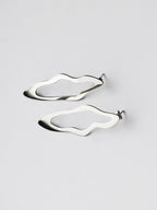 Pair of unique, organic-shaped silver stud earrings on a light gray background