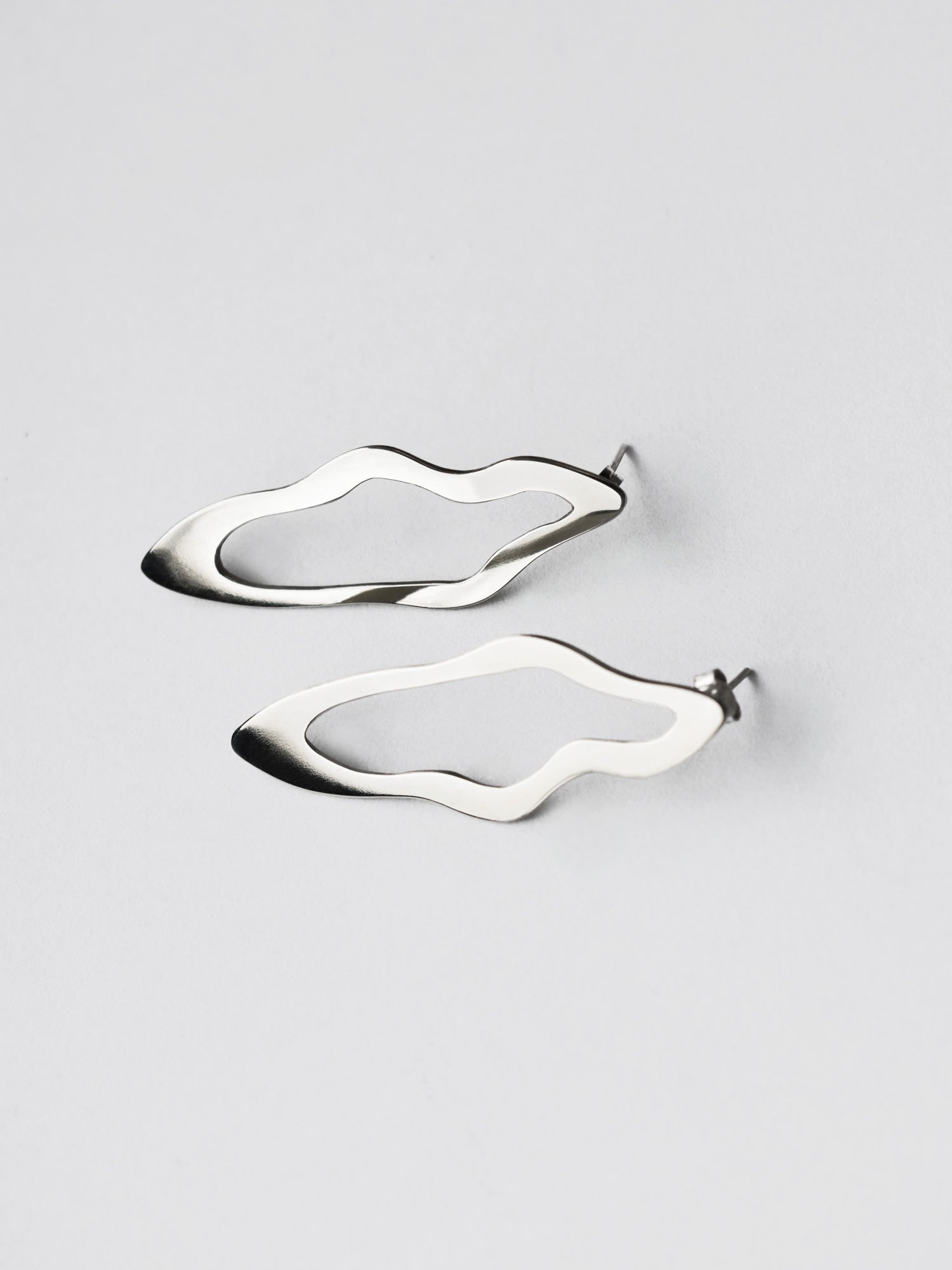 Pair of unique, organic-shaped silver stud earrings on a light gray background