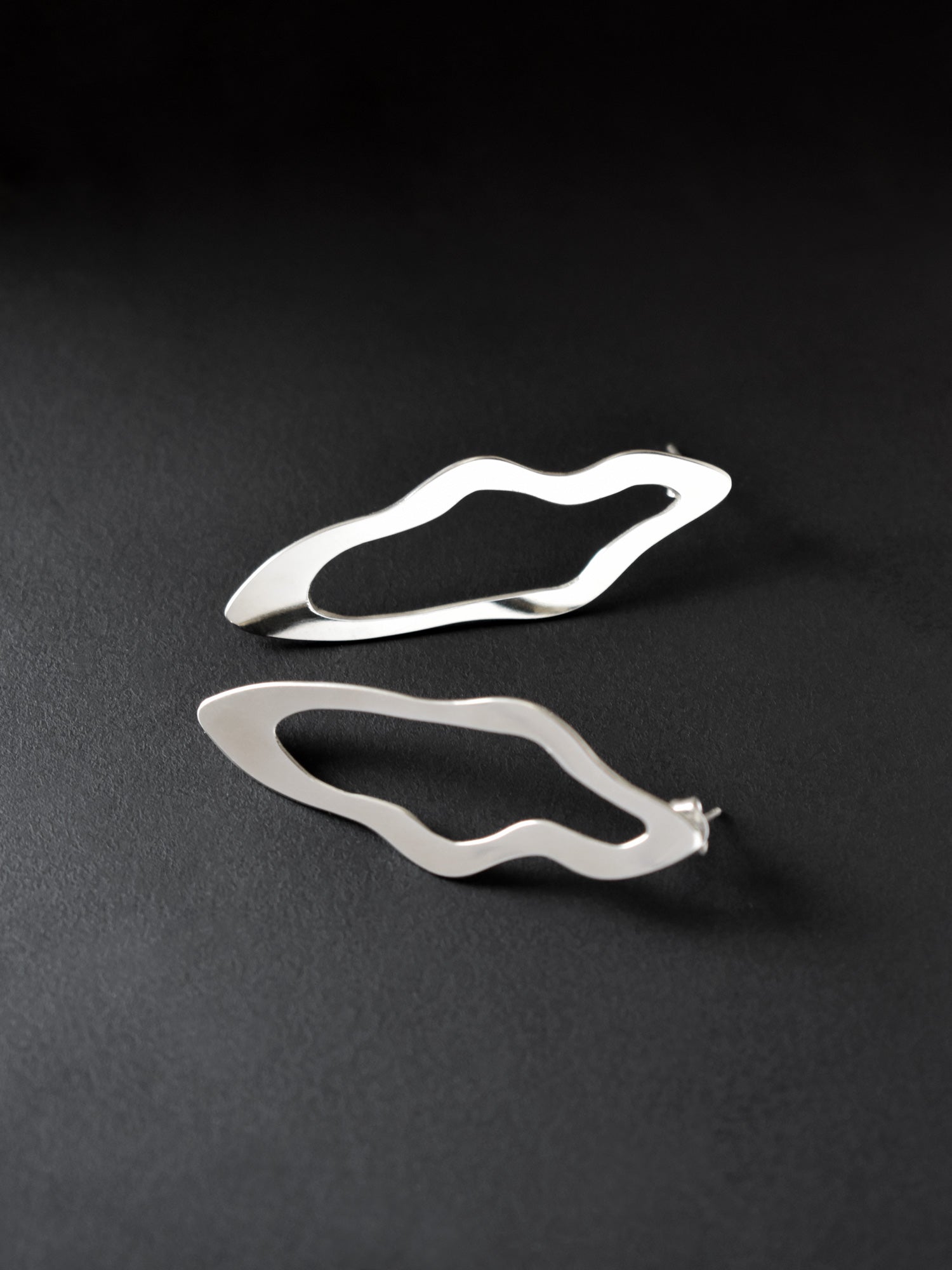 Pair of unique, organic-shaped silver stud earrings on a dark background
