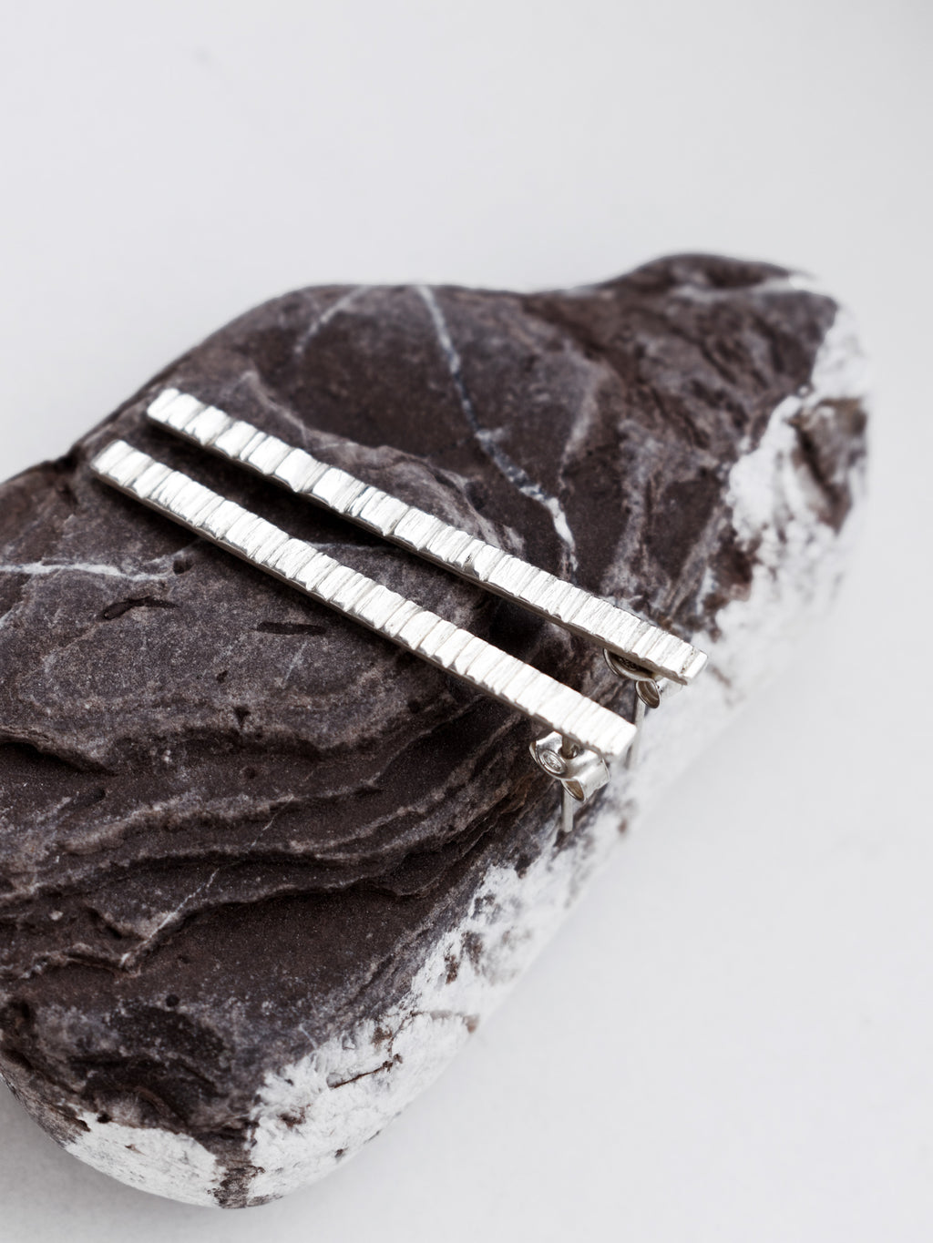 Pair of textured silver bar stud earrings on a textured stone surface