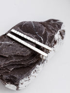 Pair of textured silver bar stud earrings on a textured stone surface